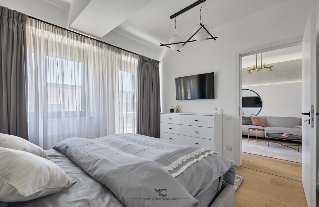 dormitor modern amenajat in tonuri de gri cu televizor si comoda